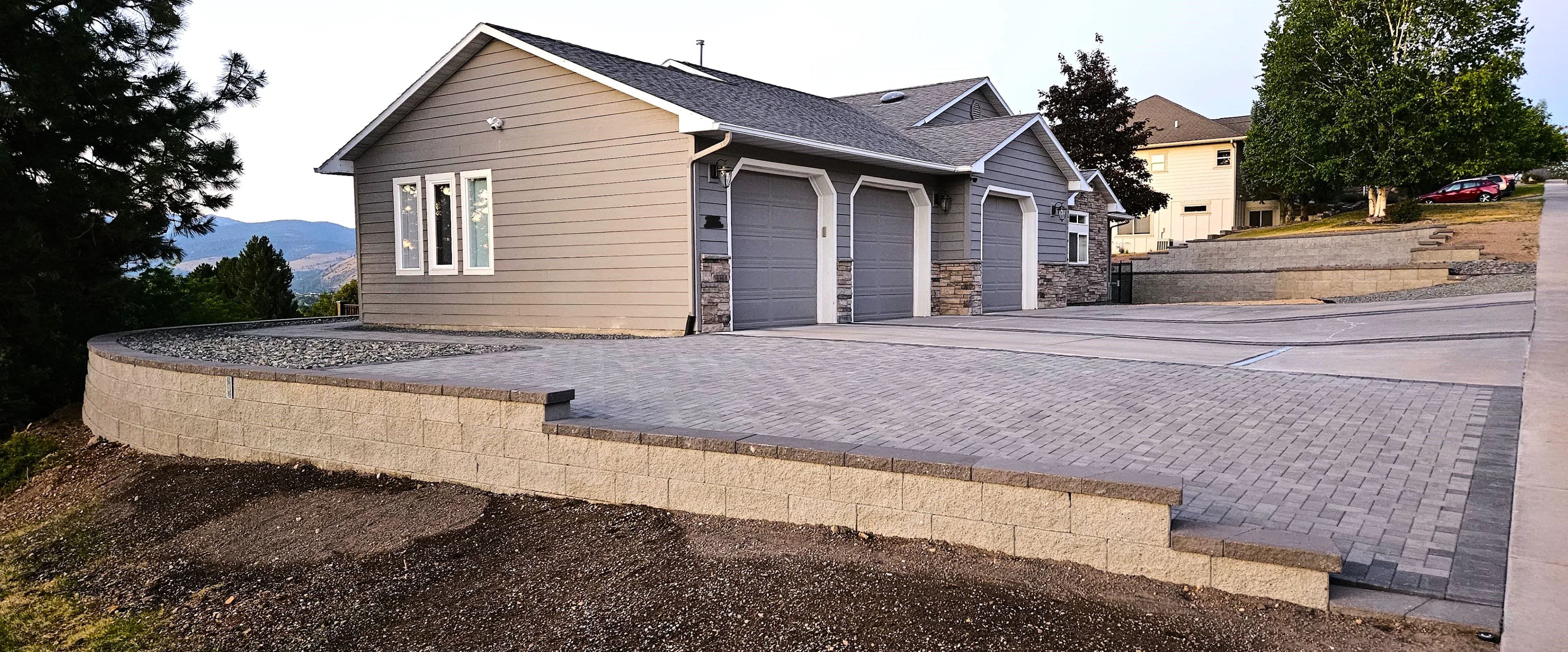 Modern gray house with stone accents and a landscaped driveway on a hillside.