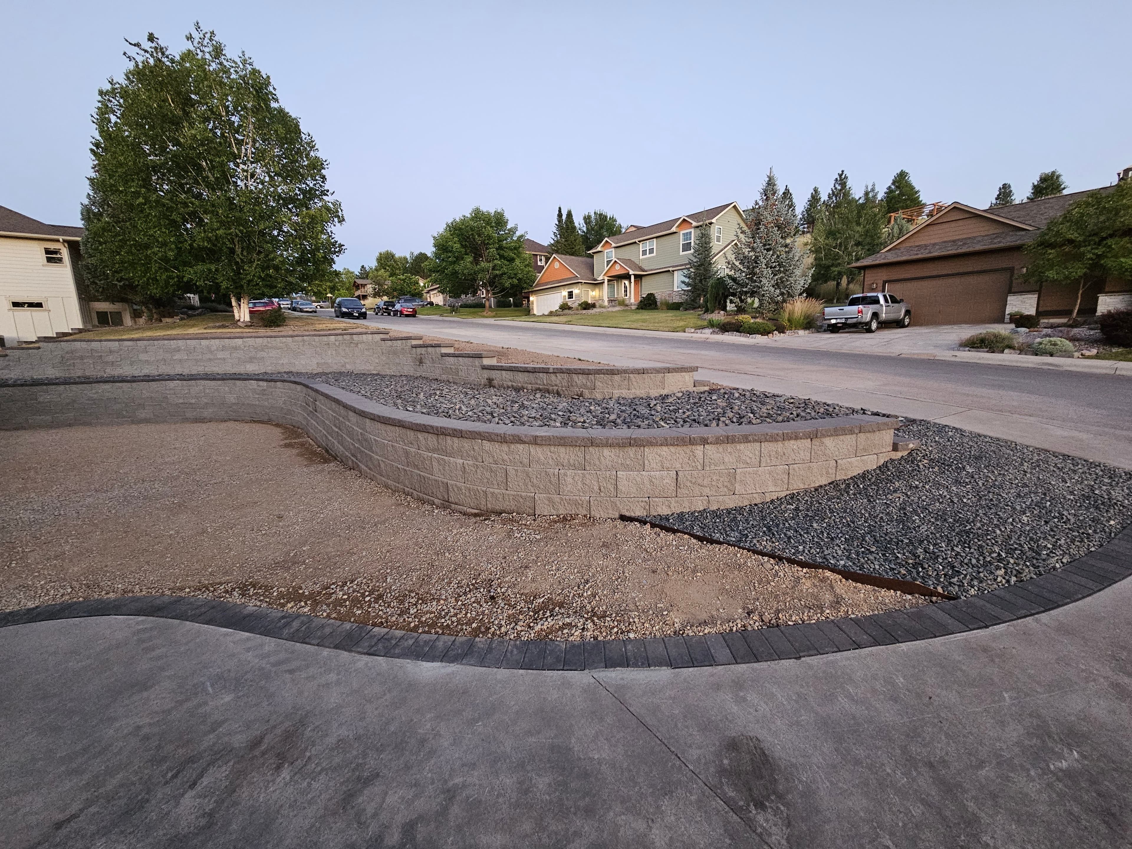 Landscaped yard with curved stone walls and gravel, residential homes in the background.