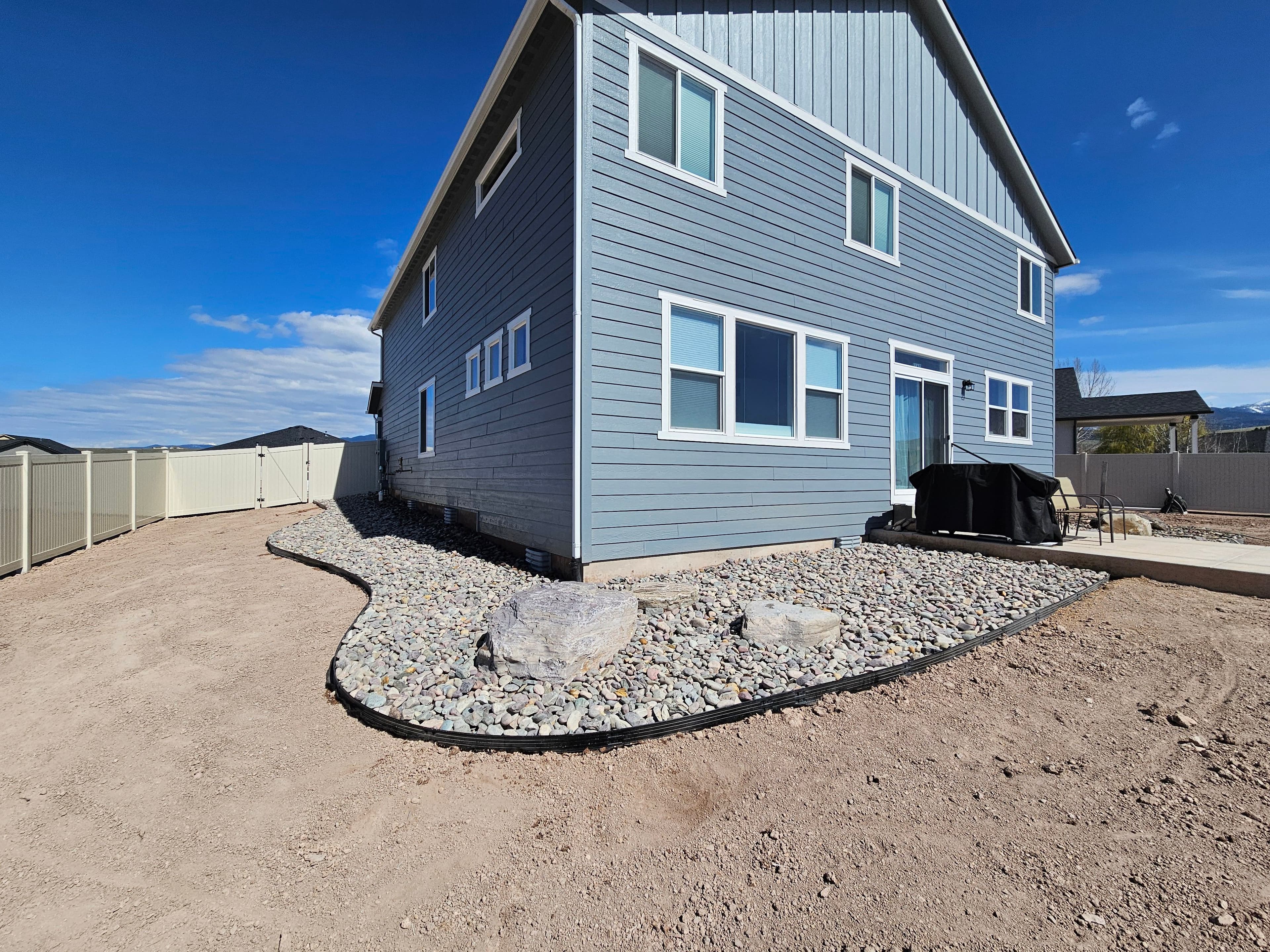 New blue home exterior with landscaped gravel yard and patio area under a clear sky.