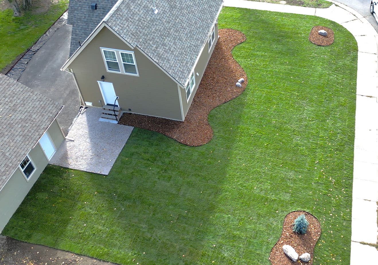 Aerial view of a landscaped yard featuring a house, fresh grass, and decorative stone beds.