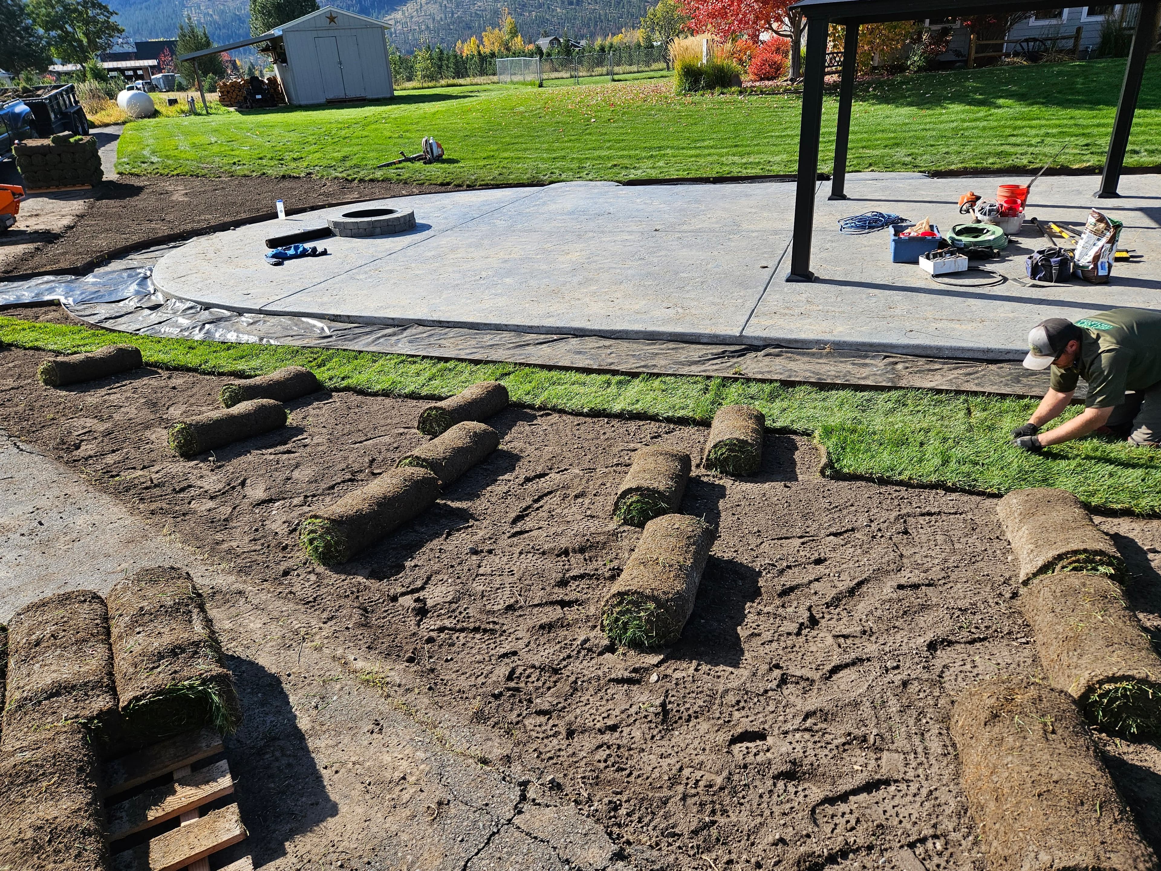 Laying fresh sod on a lawn, with tools and equipment arranged around a concrete patio.