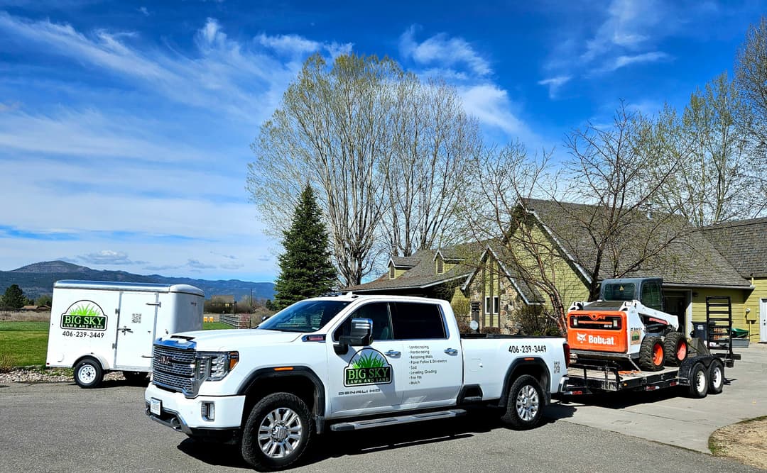 Big Sky landscaping truck with trailer and Bobcat near a house and tree-lined scenery.