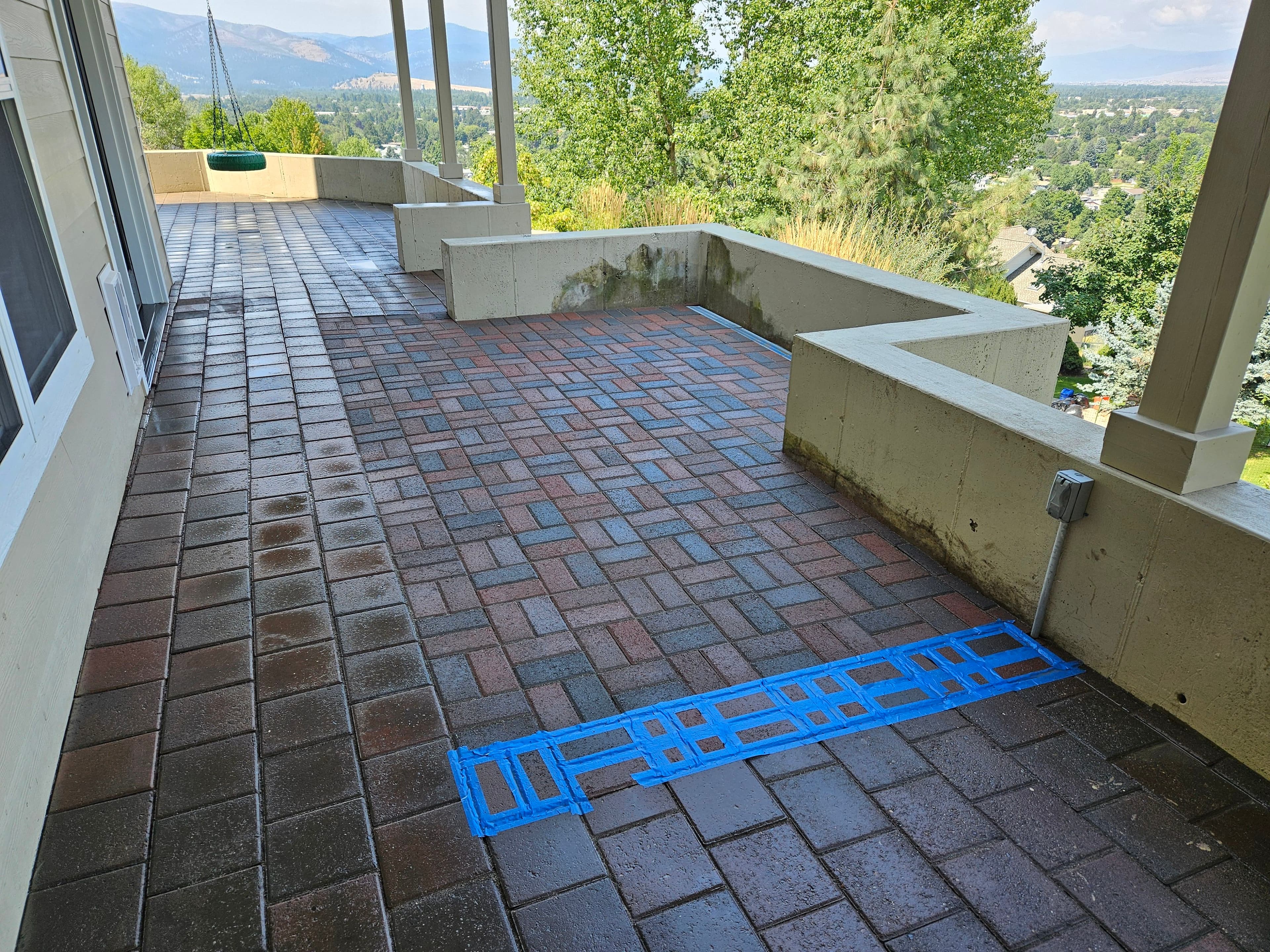 Paved patio area with blue tape marking, overlooking a scenic landscape.