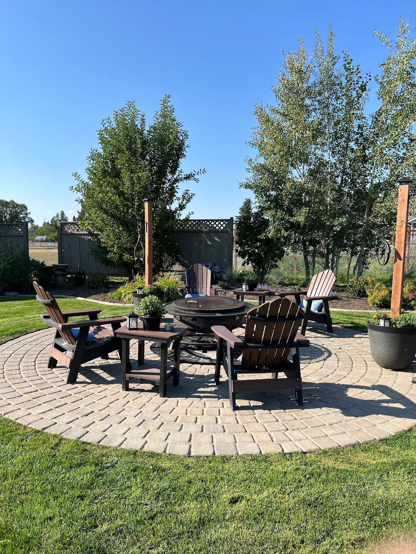 Cozy outdoor fire pit area with wooden chairs, surrounded by trees and lush green grass.