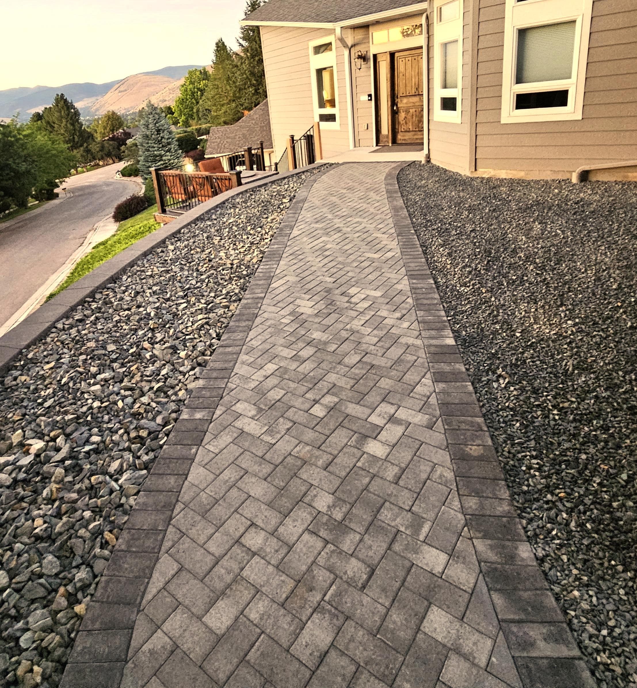 Herringbone-patterned pathway leading to a house with landscaping and mountain views.