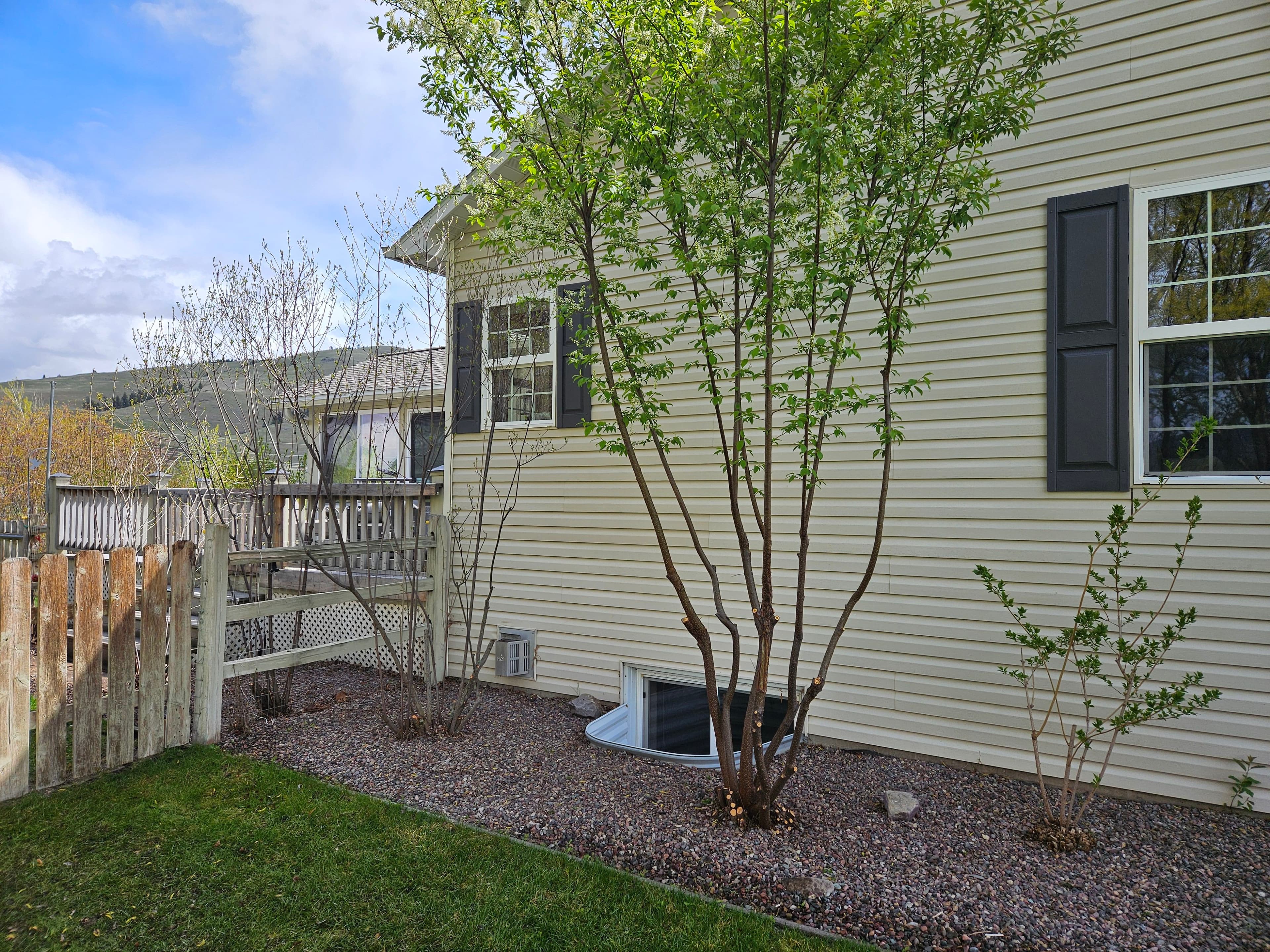 Side view of a house with lush greenery, gravel landscaping, and a wooden fence.