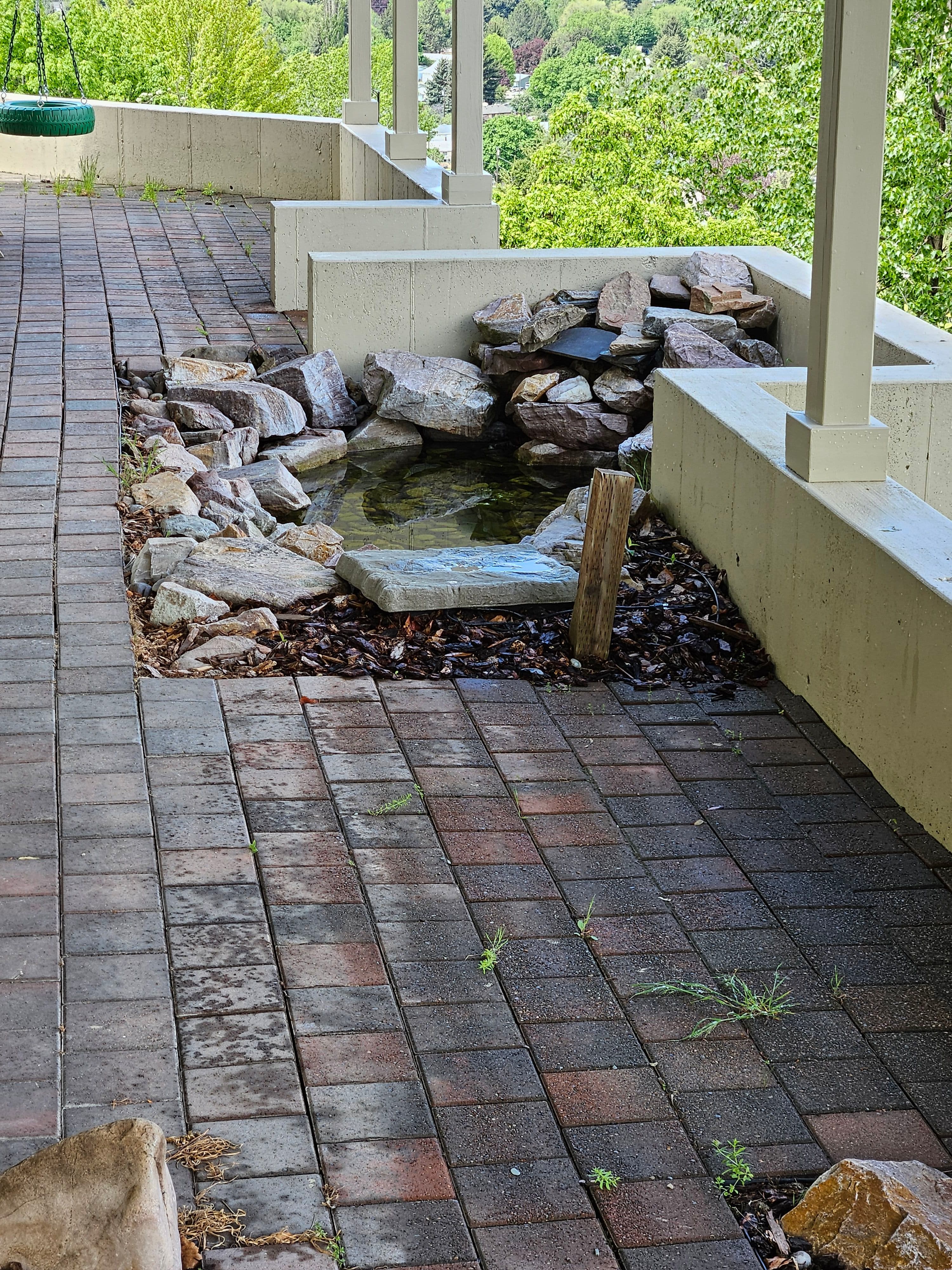 Patio pathway with stone water feature and surrounding greenery in a scenic outdoor setting.