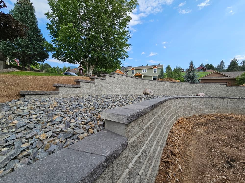 Terraced landscaping with stone walls and gravel; residential homes in the background.