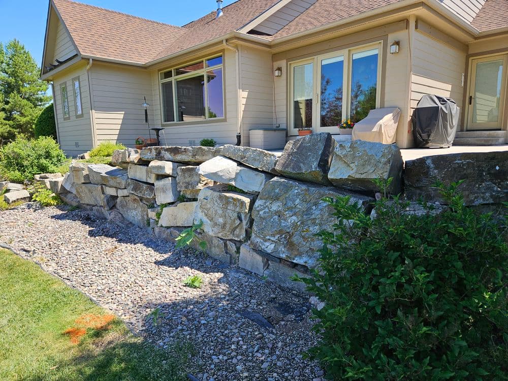 Stone retaining wall beside a modern home with landscaped garden and patio area.