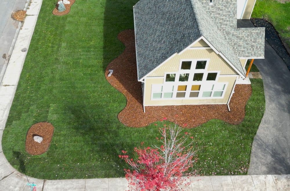 Aerial view of a house with landscaped yard featuring mulch, grass, and autumn foliage.