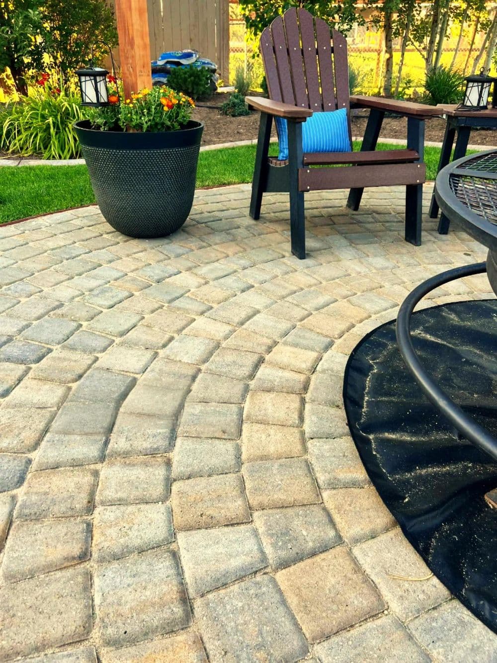 Paved patio featuring curved stone design, garden plants, and wooden chair in backyard setting.
