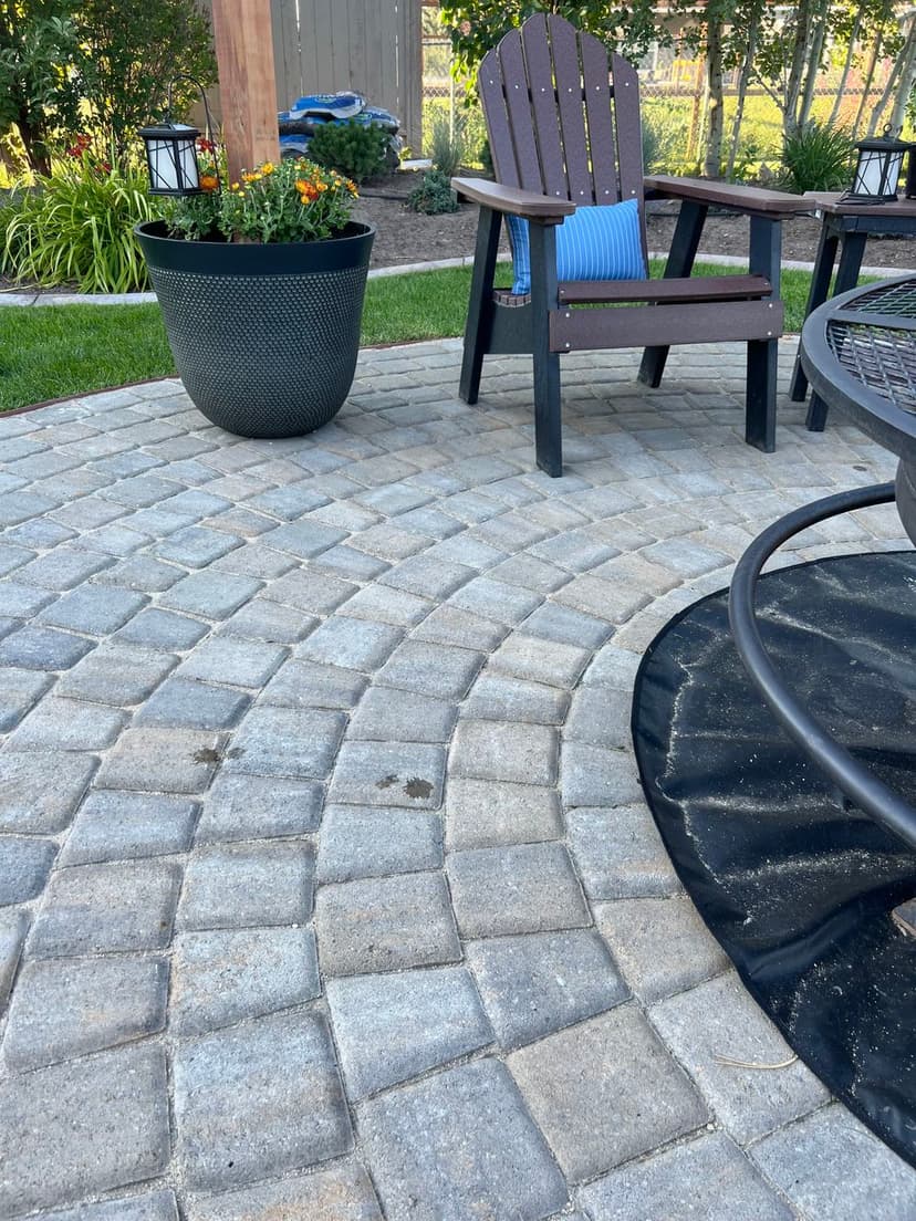 Paved patio with curved stone design, black chair, and potted plants for outdoor relaxation.
